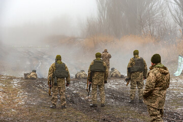 Soldiers in bulletproof vests and helmets on target practice with machine guns on a foggy day.