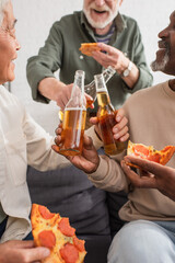 Interracial senior friends holding beer bottles and pizza at home.