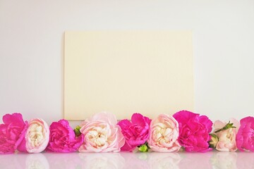 一列に並んだ赤とピンク色のカーネーションの花を添えた母の日のイメージのメッセージカードのモックアップ