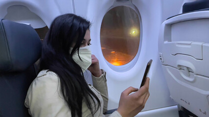 Concept traveler, vacations, passenger, airplane. Adult female tourist using her cell phone in the cabin of a commercial airplane before starting the flight to begin her vacation.