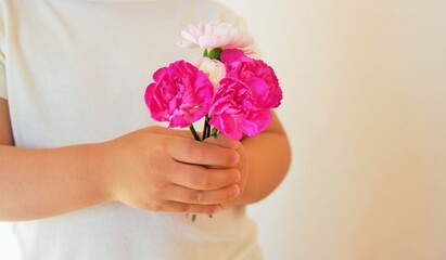 赤とピンクのカーネーションの花束を持つ子どもの手元