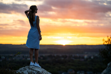 Dark silhouette of a young woman in summer dress standing outdoors enjoying view of nature at sunset
