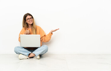 Young woman with a laptop sitting on the floor holding copyspace imaginary on the palm to insert an...