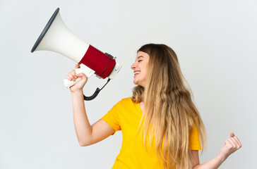 Young blonde woman isolated on white background shouting through a megaphone to announce something in lateral position