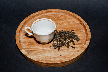 Dry tea with green leaves in wooden spoons, on black background.