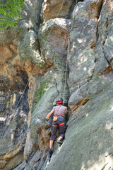 Young man climbing steep wall of rocky mountain. Male climber overcomes challenging route. Engaging...