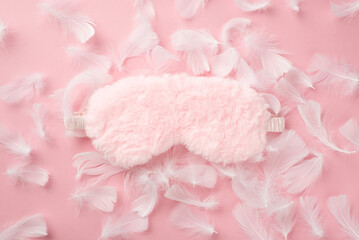 Fototapeta na wymiar Top view photo of pink fluffy sleeping mask and feathers on isolated pastel pink background with copyspace