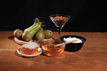 Liquid honey and honeycombs, almond nuts, green pears on the table