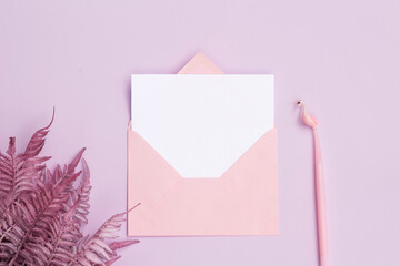Blank white paper in pink envelope with flowers and pink pen on lilac - pink background.
