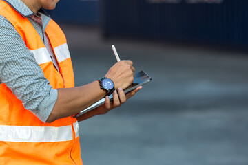 Foreman or worker hand holding tablet for writing and checking in goods in container at Container cargo site.