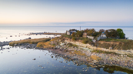 Aerial sunset colored view to the thin cape badly suffering by coastal erosion and with the abandoned historic guard station buildings, nearly to collapse to the sea. Concept of coastal erosion