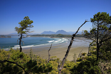 Aerial view of Cox Bay beach in Tofino with ocean waves and mountains in background during low tide. - obrazy, fototapety, plakaty