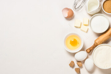 Baking ingredients at white table. Flour, brown sugar, milk, eggs and utensils. Top view with copy...