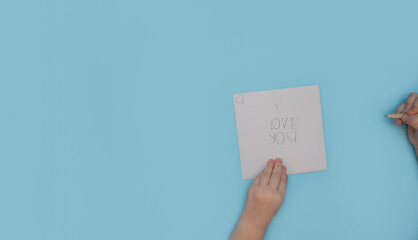 Little girl writing I love you on white paper, isolated on blue background