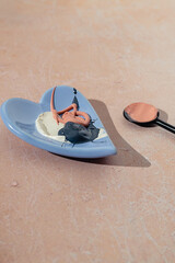 Pink, white and black mud clay mask cream smudge or smear mixed in a blue plate and a spoon on a pink background. Natural beauty skin care cosmetic product. Flat lay. Facial spa treatment routine.