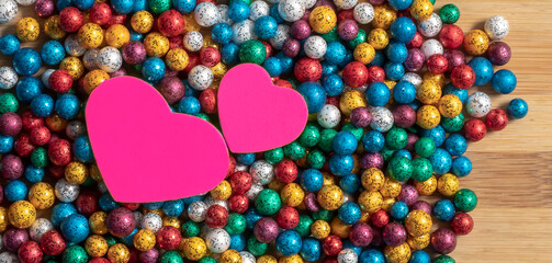 Valentine's Day background. Multicolor small size thermocol decorative balls with two pink hearts on top of a wooden table - obrazy, fototapety, plakaty