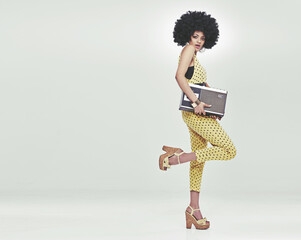 Time to disco. A young woman wearing a 70s retro jumpsuit holding a cassette player and striking a...