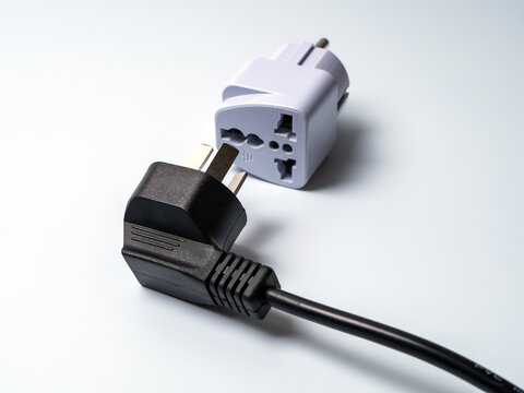 An electrical plug lying next to an adapter for another type of electrical plug.