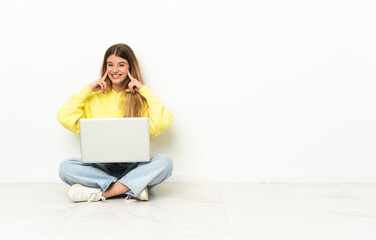 Fototapeta premium Young woman with a laptop sitting on the floor smiling with a happy and pleasant expression