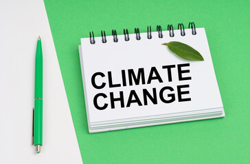 On a white-green background lies a pen, a leaf of a plant and a notepad with the inscription - Climate Change