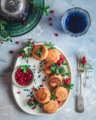 Breakfast set. Russian cheese cakes on a craft ceramic plate with lingonberry over a blue background