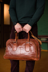 close-up photo of orange leather travel bag in mans hands