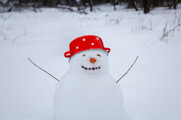 Funny snowman in a red soup pot with white dots instead of a hat, a cute snowman stands in a winter village, snow-covered trees