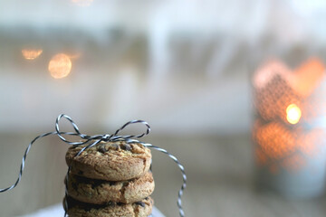Stack of chocolate chip cookies, tied with ribbon. Lit candle and bokeh lights in the background. Selective focus.