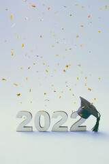 Graduation 2022 wearing graduate hat on a wooden 2022 number with flying confetti