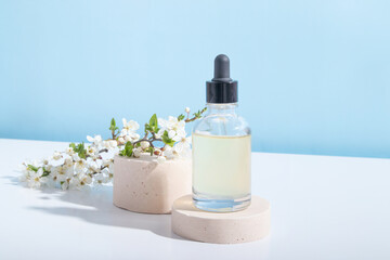 Obraz na płótnie Canvas Glass dropper bottle with face serum on pedestal with blooming twigs on a beige background. Horisontal stock photo