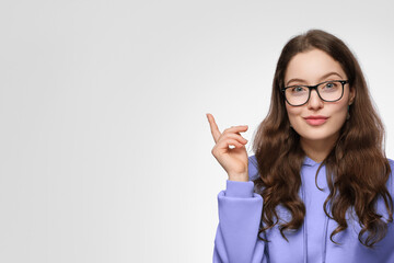 A smiling teenage girl with long hair and glasses. The girl is wearing a violet oversized sweatshirt, pointing up.