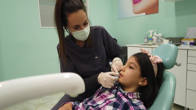 Dentist examines the mouth of an 8-year-old girl, touching mouth and teeth