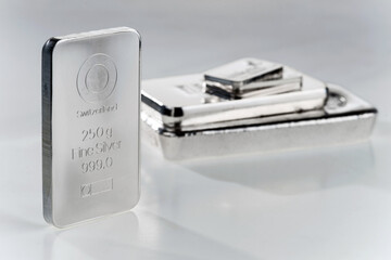 Minted silver bar against a background of a stack of various silver ingots. Selective focus..
