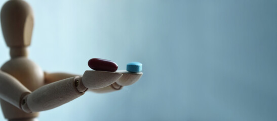 Wooden figurine of a man, holding two pills, on a light background with free space for your text. Medicine and healthcare concept.