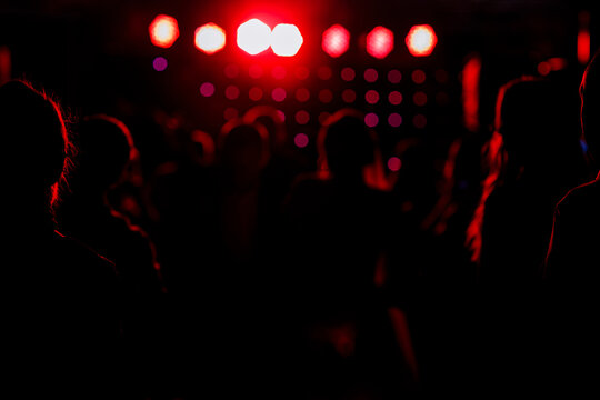cheering crowd in front of bright red stage lights. Silhouette image of people dance in disco night club or concert at a music festival.