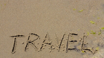 Travel concept - inscription in the sand. Sandy coast of the sea. Motivation. Ocean wave. The word travel is written on the sea beach. Vacations on the shore