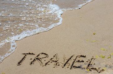Travel concept - inscription in the sand. Sandy coast of the sea. Motivation. Ocean wave. The word travel is written on the sea beach. Vacations on the shore