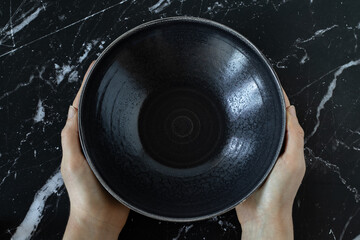 Fasting Christian biblical concept. Woman's hands holding an empty dish bowl on a black textured...