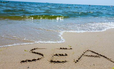 The inscription sea on the sand by the water and the rising wave, seashore beach vacation by the sea