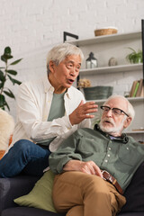 Elderly asian man talking near friend on couch at home.