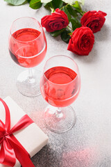 Two wine glasses with red wine for romantic dating or Valentine's day dinner with red rose on gray background. Vertical format.