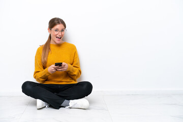 Young caucasian woman sitting on the floor isolated on white background surprised and sending a message