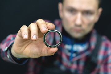 A young guy holds a bearing in his hand on a black background. A bicycle mechanic in the workshop changes bearings for the steering column. Repair of motorcycles and cars in the service center.