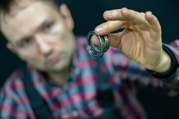 A young guy holds a bearing in his hand on a black background. A bicycle mechanic in the workshop changes bearings for the steering column. Repair of motorcycles and cars in the service center.