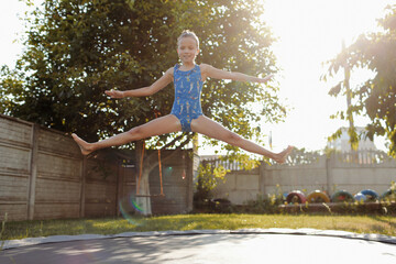 little sports girl jumps on a trampoline. Outdoor shot of girl jumping on trampoline, enjoys...