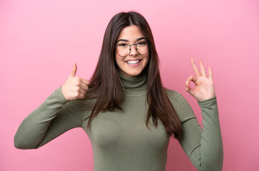 Young Brazilian woman isolated on pink background With glasses and doing OK sign