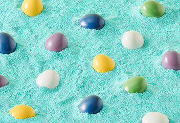 Pattern made of colorful Easter eggs on turquoise sand. Creative holiday background.  Minimalan natural concept.