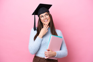 Young student Brazilian woman wearing graduated hat isolated on pink background looking up while...