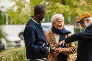 Fototapeta na wymiar Happy senior man talking to multicultural friends in autumn park.