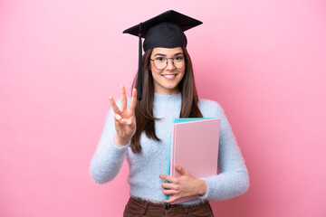 Young student Brazilian woman wearing graduated hat isolated on pink background happy and counting three with fingers